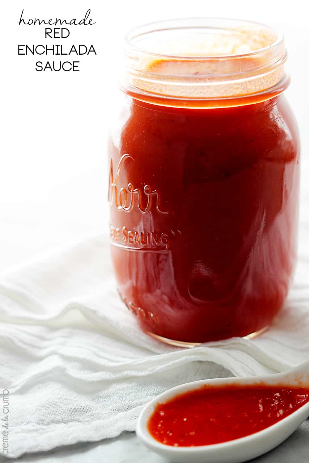 homemade red enchilada sauce in a mason jar with a spoon full of sauce with the title of the recipe written on the top left corner of the image.