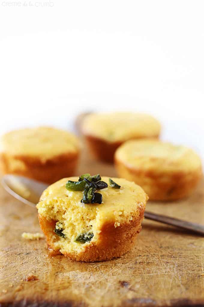 a honey poblano corn muffin with a bite taken out of it with a spoon and more muffins faded in the background.