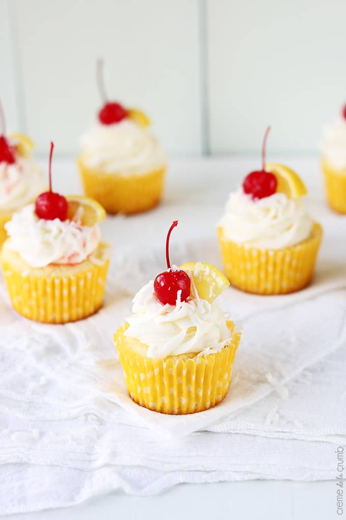 lemon coconut cupcakes topped with cherries and slices of lemon.