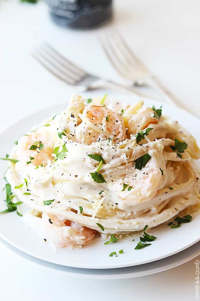 close up of shrimp fettuccine Alfredo on a plate with two forks faded in the background.