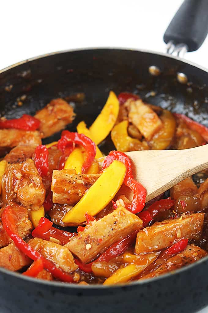 mango chicken stir fry and a wooden serving spoon in a skillet.