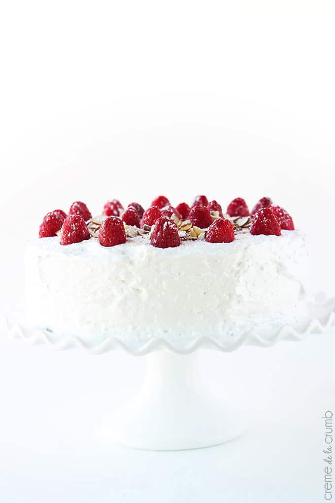 chilled raspberry almond cake topped with raspberries and slivers of almonds on a cake stand.