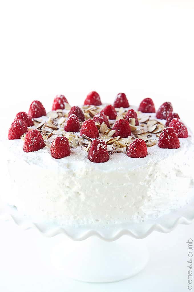 chilled raspberry almond cake topped with raspberries and slivers of almonds on a cake stand.