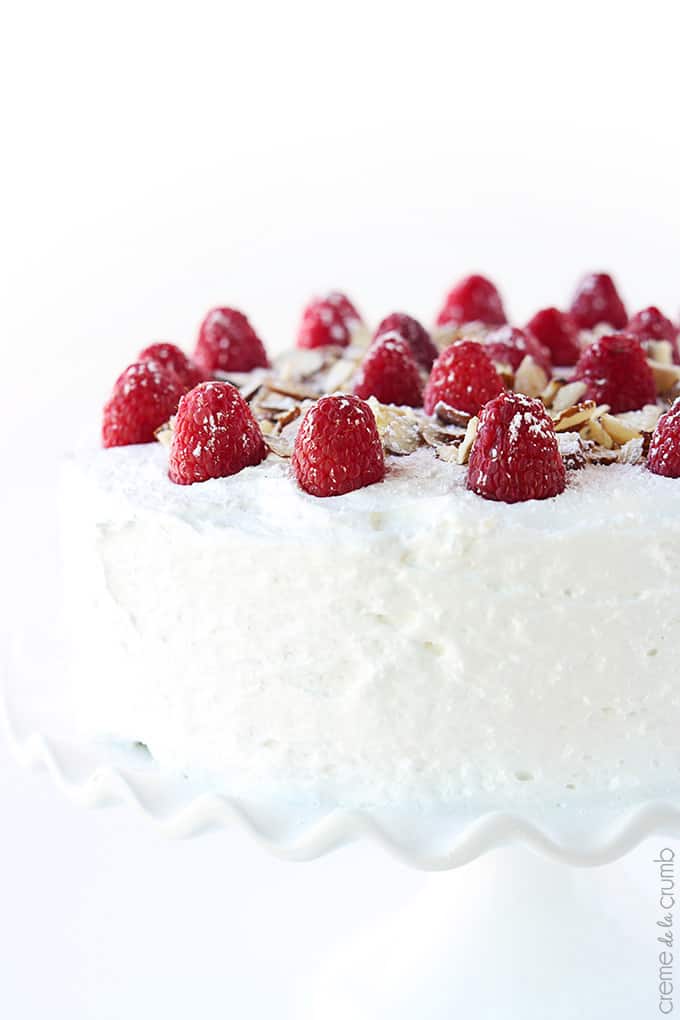 close up of chilled raspberry almond cake topped with raspberries and slivers of almonds on a cake stand.
