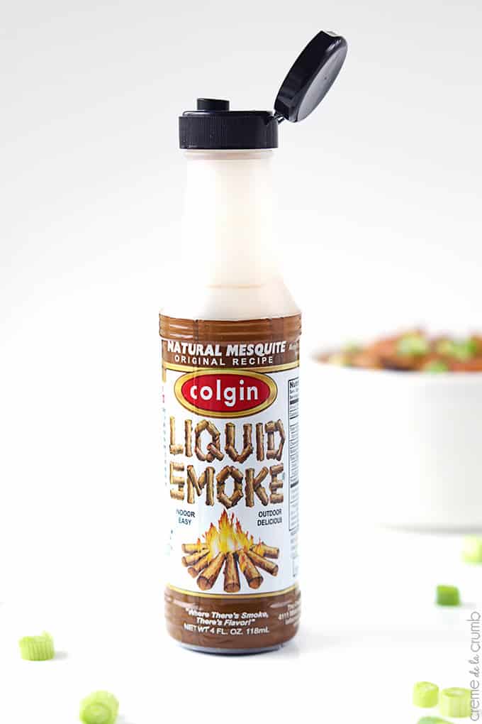 a bottle of liquid smoke with smokey bbq baked beans in bowl faded in the background.