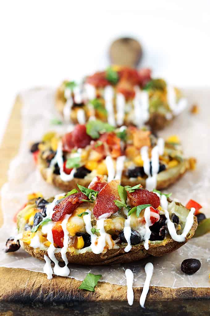 Southwest loaded potato skins lined up on a wooden cutting board.