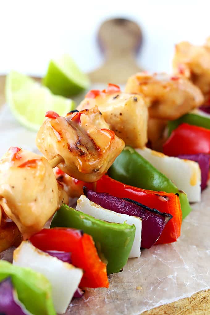 close up of bang bang chicken kabobs on a wooden cutting board with slices of lime.