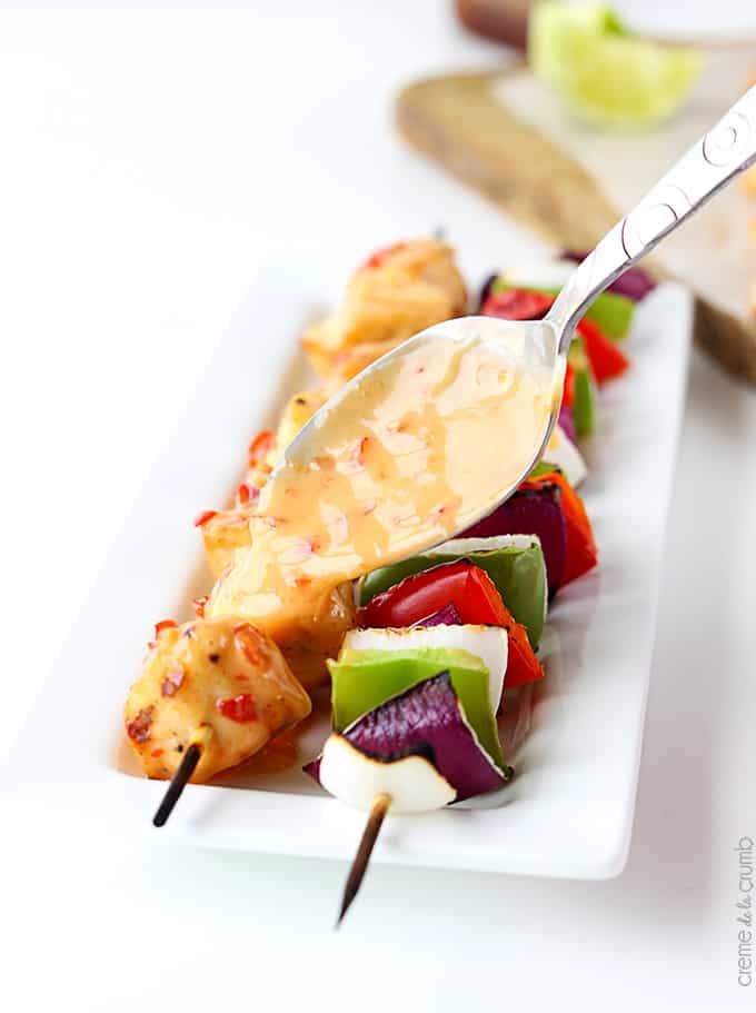 bang bang chicken kabobs on a plate with a spoon pouring sauce on top of them.