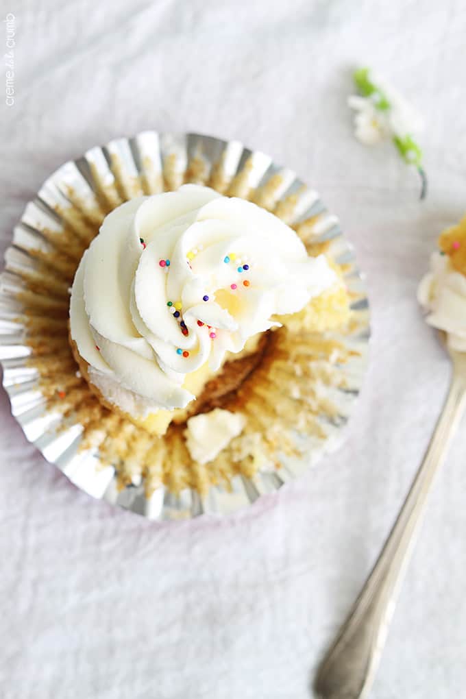 top view of a birthday cake cupcake with its liner open and a bite taken from it with a fork on the side with the bite on it.