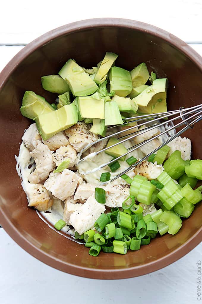 top view of a bowl full of chicken, avocado, celery and green onions with a whisk.