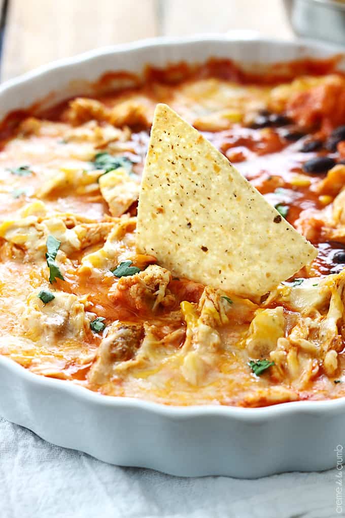 close up of chicken enchilada dip in a serving dish with a chip dipped in it.