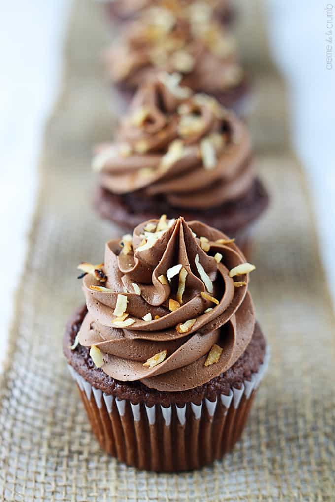 chocolate coconut cupcakes lined up on a burlap table runner.