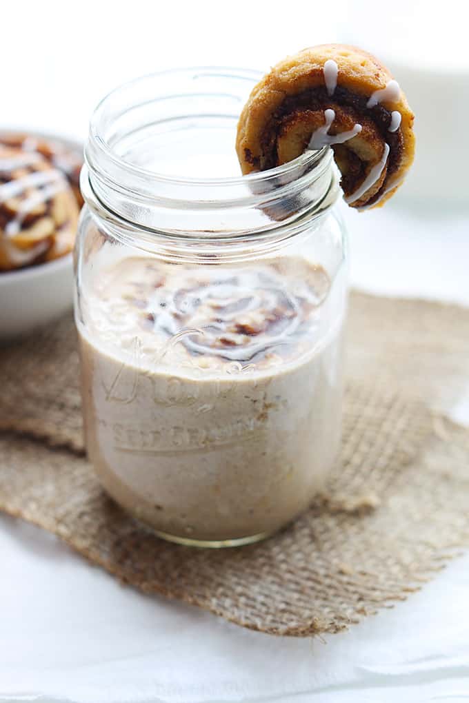 cinnamon roll overnight oats in a mason jar with a cinnamon roll straddling the top of the jar.