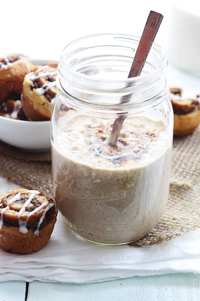 cinnamon roll overnight oats with a spoon in a mason jar with small cinnamon rolls on the side.
