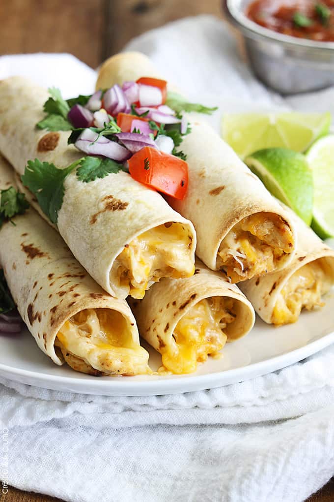 slow cooker cream cheese chicken taquitos on a plate on a white cloth napkin with slices of lime.