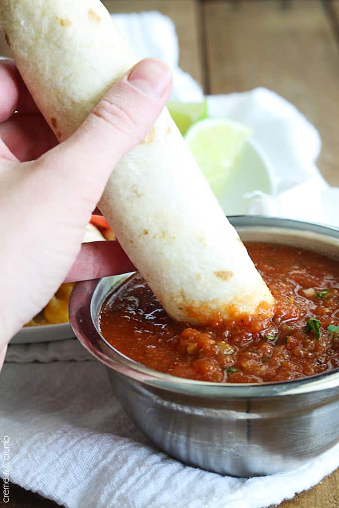 a hand dipping a slow cooker cream cheese chicken taquito in salsa.