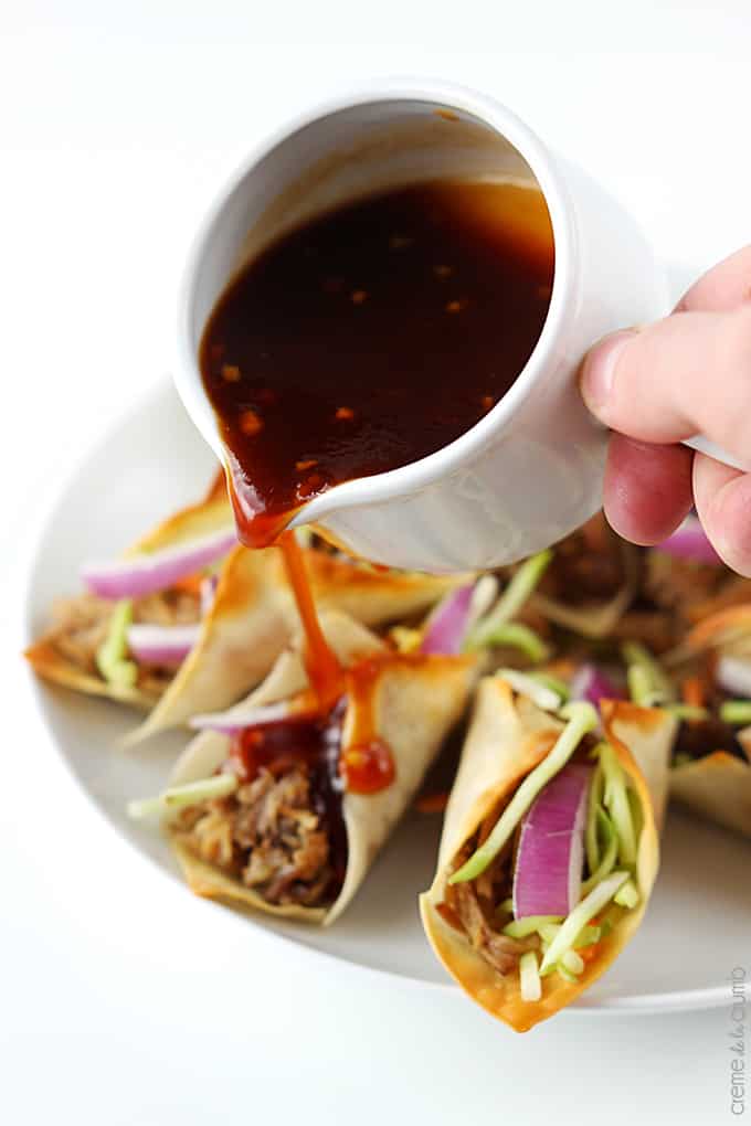 a hand pouring sauce on Hawaiian bbq pork wonton tacos on a plate.