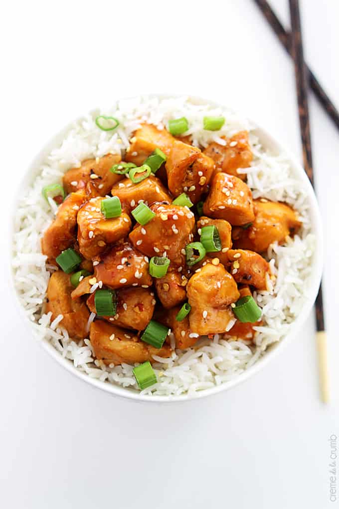 top view of orange chicken on rice in a bowl with chopsticks on the side.