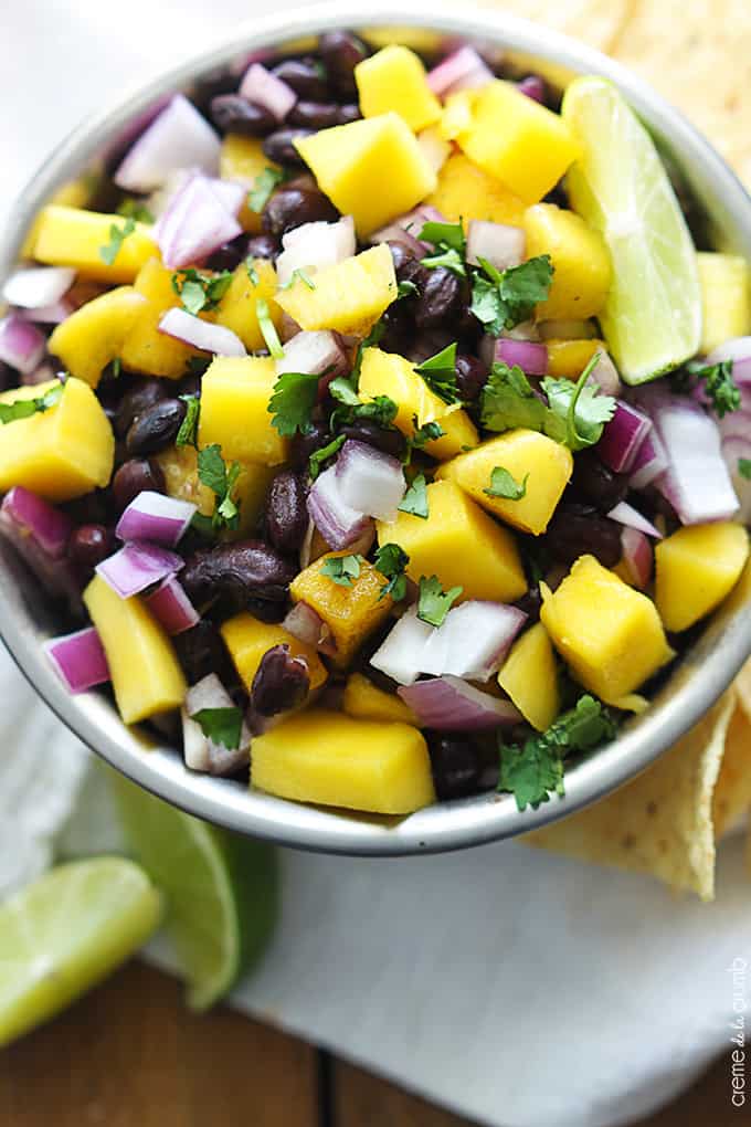 top view of mango black bean salsa in a bowl with limes and chips on the side.