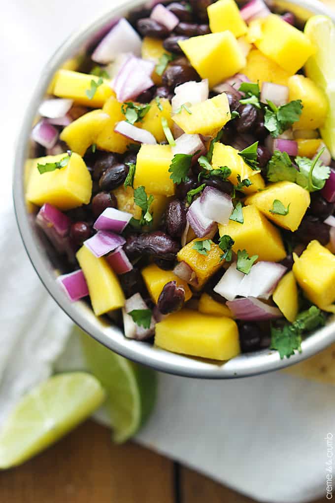 up close top view of mango black bean salsa in a bowl with slices of limes on the side.