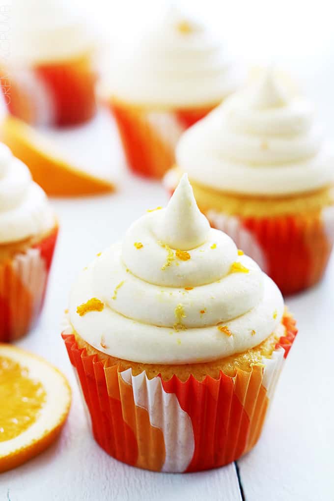 an orange cream cupcake with an orange slice next to it with more cupcakes faded in the background.