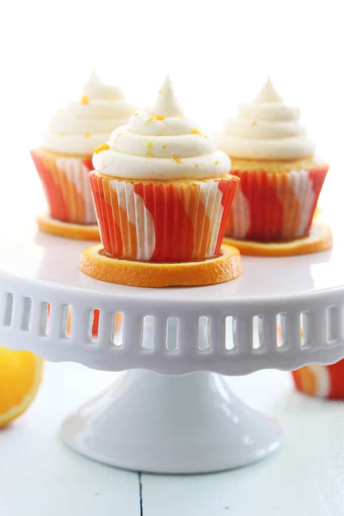 orange cream cupcakes on orange slices on a pedestal cake stand.