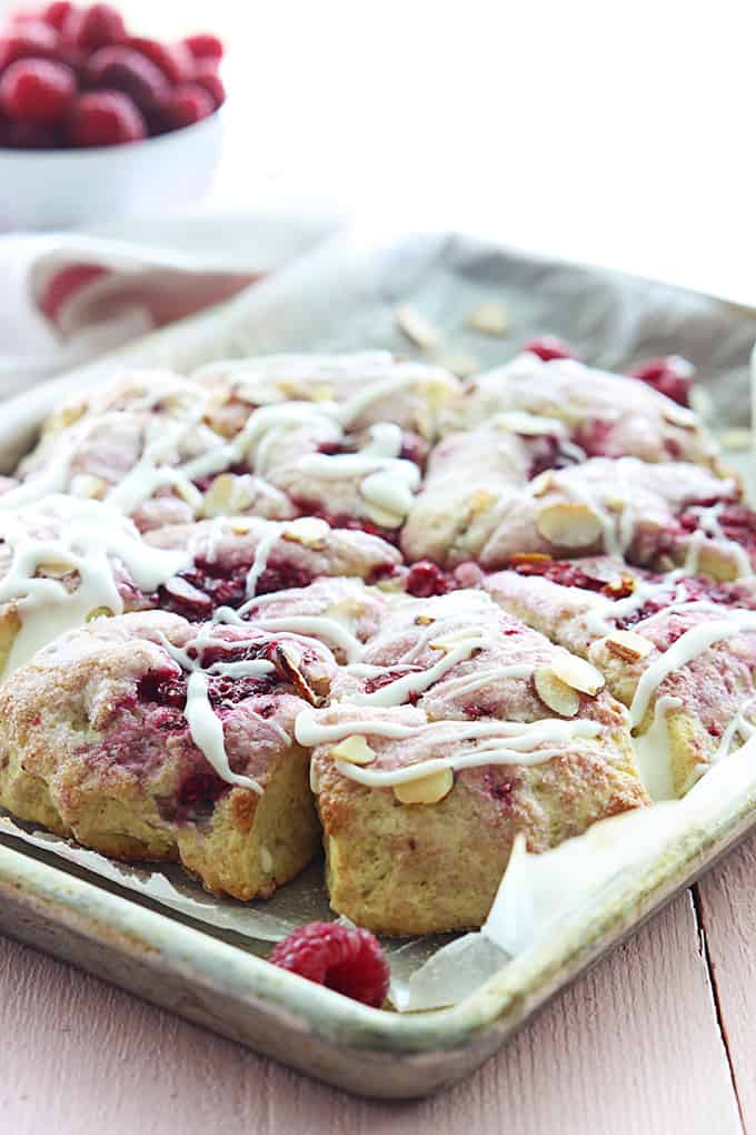 raspberry almond scones with almond glaze on a baking sheet.