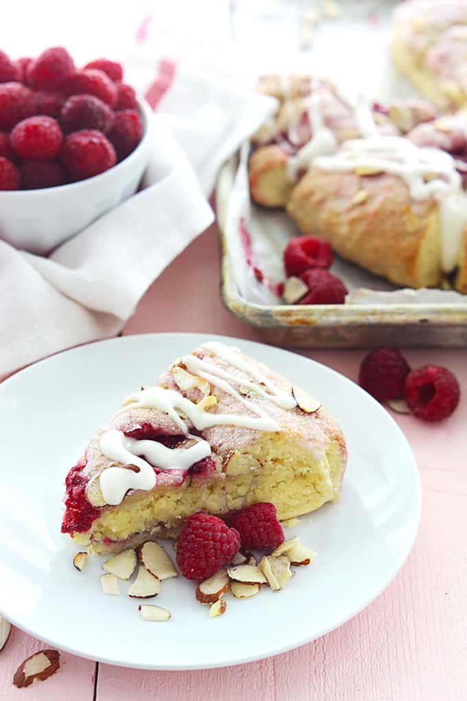 a raspberry almond scone on a plate with more scones on a baking sheet and a bowl of raspberries in the background.