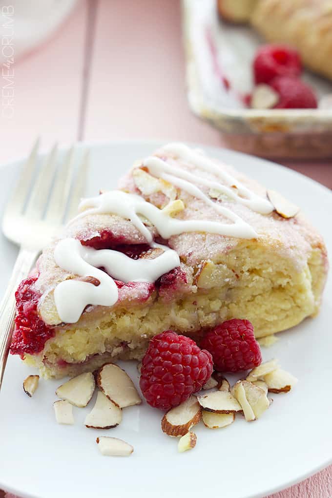 a raspberry almond scone on a plate with a fork, almond slices and raspberries on the side.