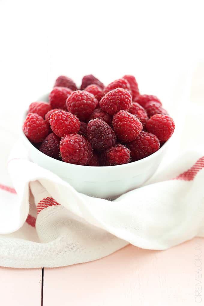 a bowl of raspberries on top of a cloth napkin.