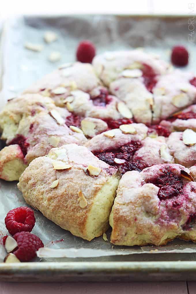 raspberry almond scones on a baking sheer with raspberries and almond slices on the side.