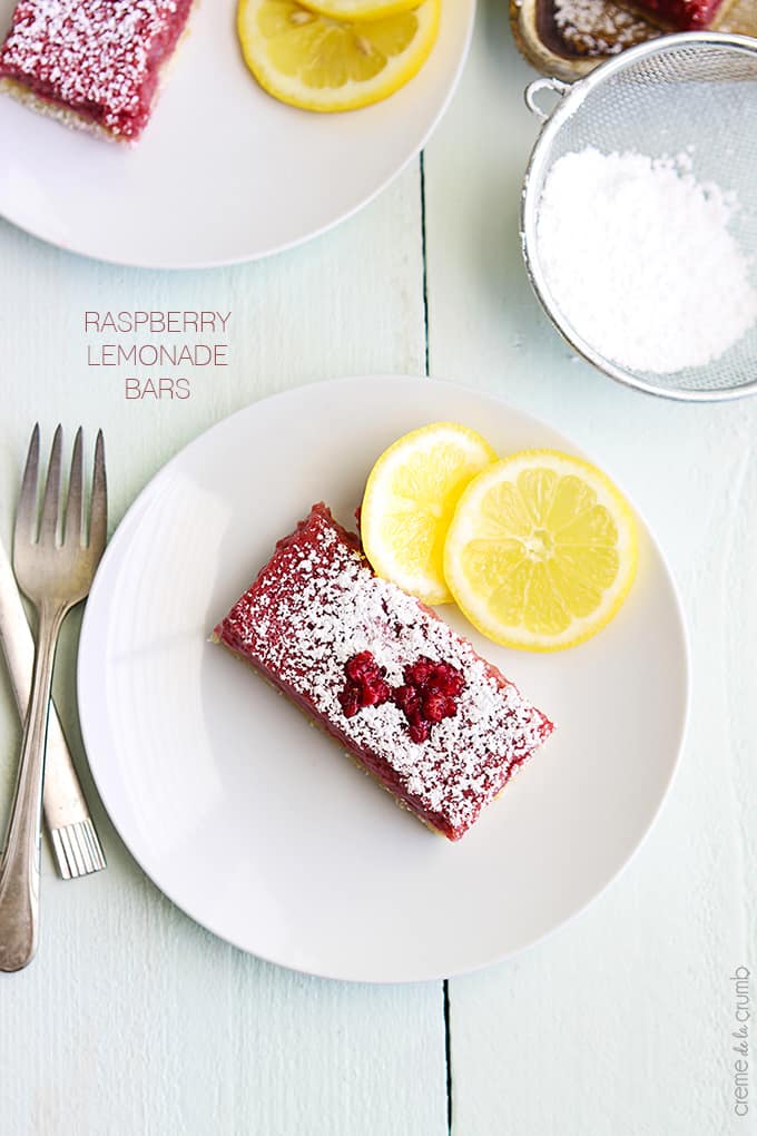 a raspberry lemonade bar with slices of lemon on the side on a plate with a fork on the table with the title of the recipe written on the left middle of the image.