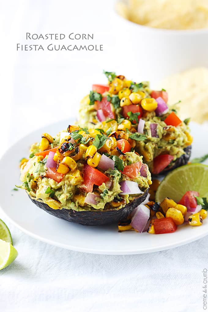 roasted corn fiesta guacamole in hallowed avocados on a plate with the title of the recipe written on the top left corner of the image.