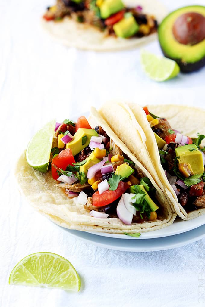 slow cooker Santa Fe chicken tacos on a plate with another taco, slices of lime and half of an avocado faded in the background.