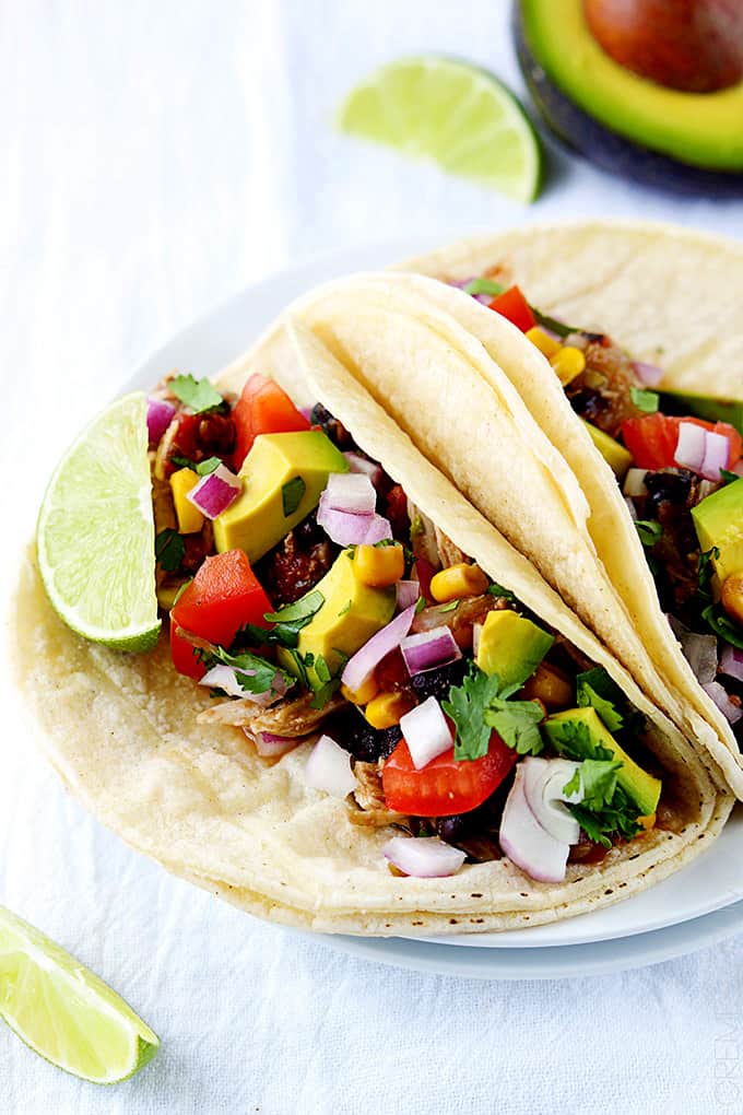 slow cooker Santa Fe chicken tacos on a plate with slices of lime and half an avocado on the side.