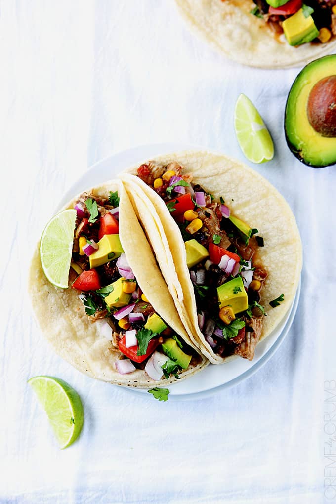 top view of slow cooker Santa Fe chicken tacos on a plate with slices of lime and a half of an avocado on the side.