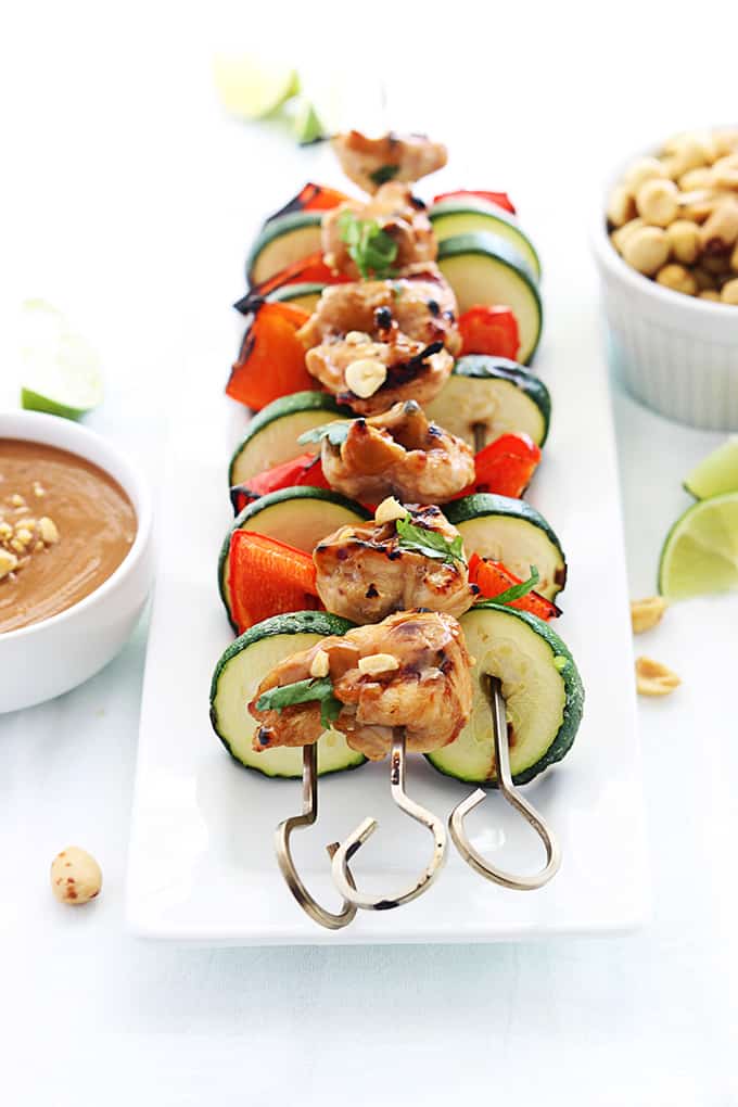 Thai peanut chicken kabobs on a plate with peanut sauce, peanuts, and slices of lime on the side.