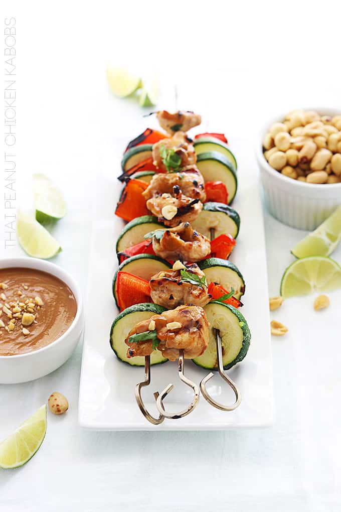 Thai peanut chicken kabobs on a plate with peanut sauce, peanuts, and slices of limes on the side.