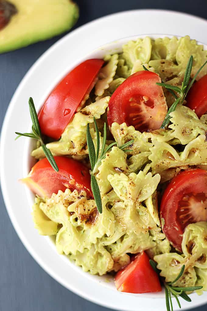 top view of a bowl of creamy avocado pasta with half of an avocado on the side.