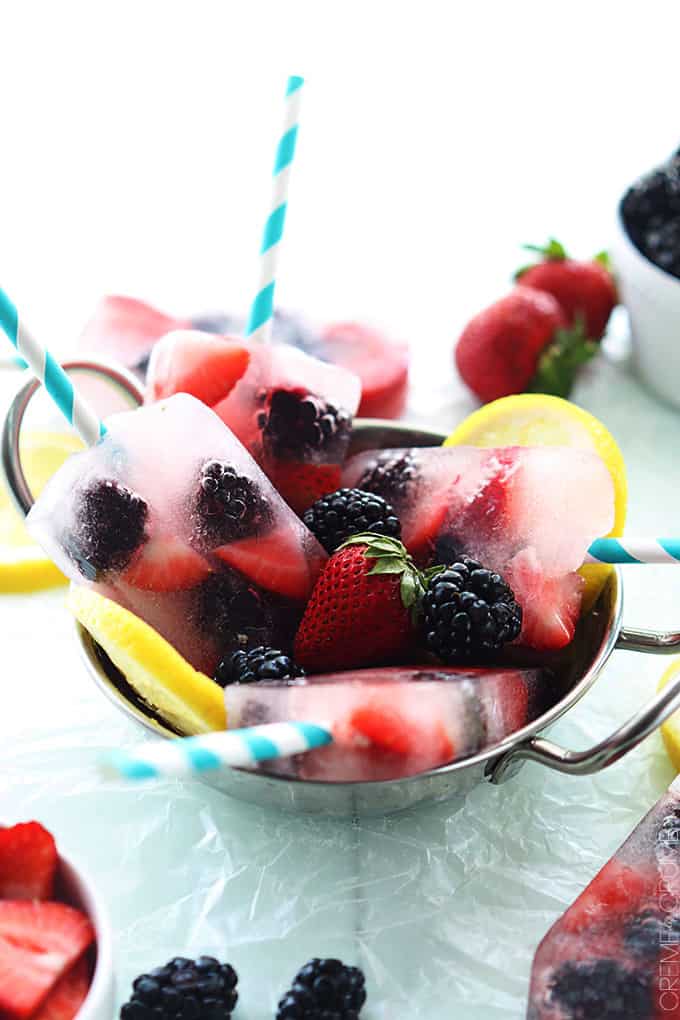 berry lemonade popsicles in a metal bowl with berries and slices of lemon.