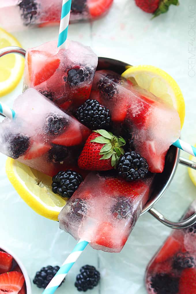 close up top view of berry lemonade popsicles with berries and slices of lemon in a metal bowl.