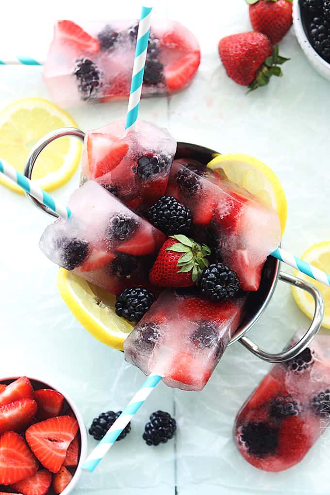 top view of berry lemonade popsicles in a metal bowl surrounded by more popsicles, berries and slices of lemon.