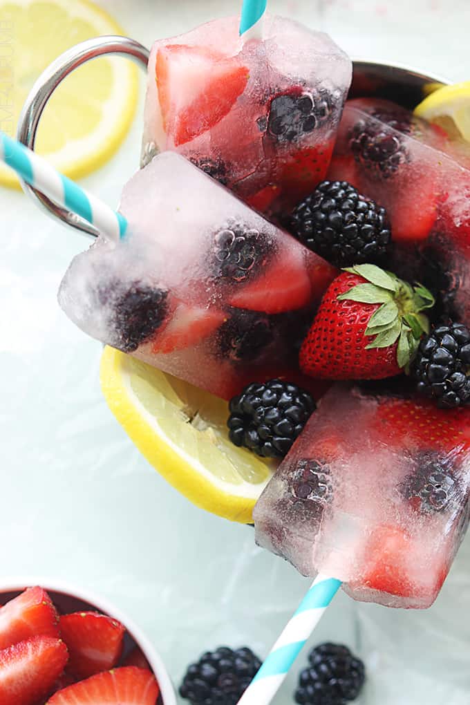 close up of berry lemonade popsicles in a metal bowl with berries and slices of lemon.