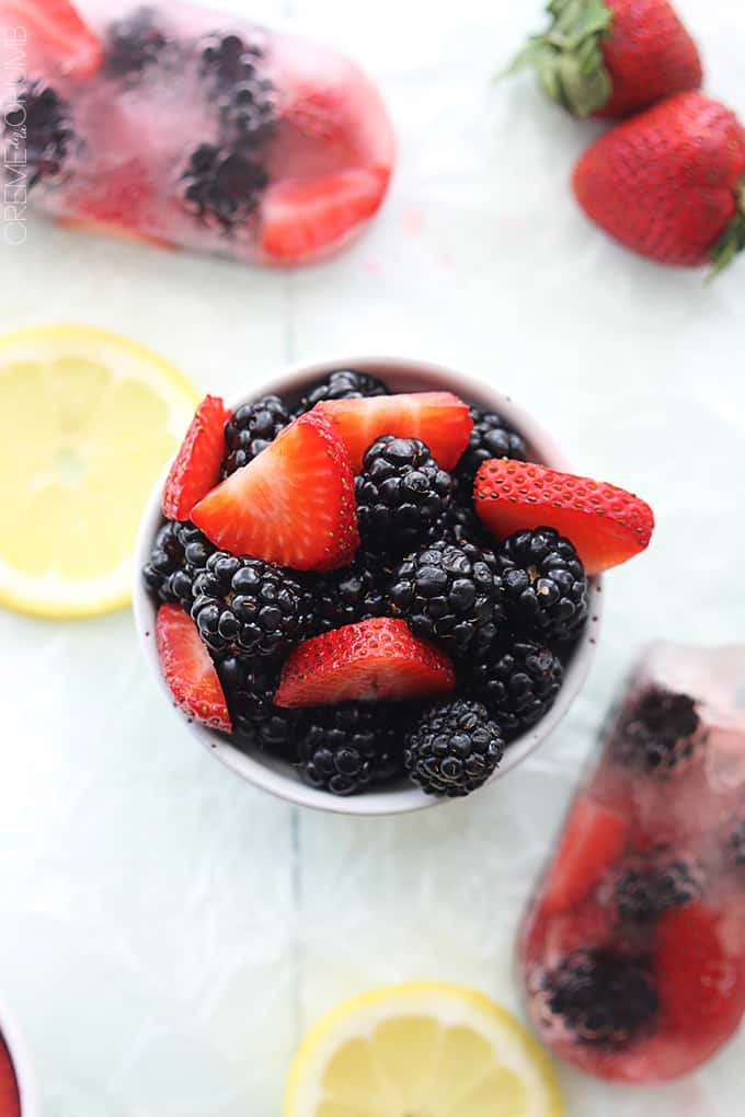 top view of berries in a cup with slices of lemon, berry lemonade popsicles, and. strawberries on the side.