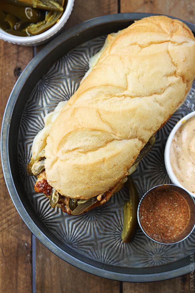 top view of a fiery jalapeño chicken melt on a serving tray with jalapeños, spices and sauce in bowls on the side.