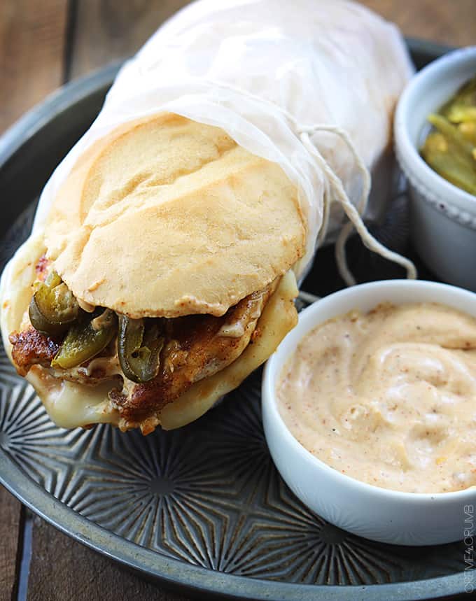 a fiery jalapeño chicken melt on a serving tray with sauce and jalapeños in bowls on the side.