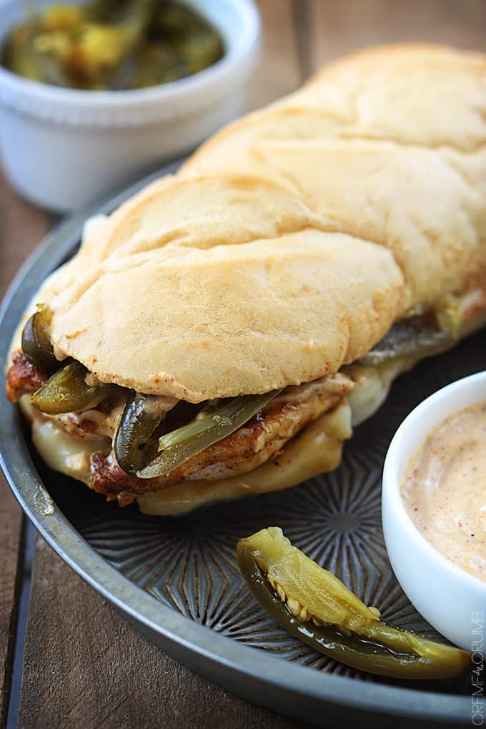 a fiery jalapeño chicken melt on a serving tray with jalapeños and sauce in bowls on the side.