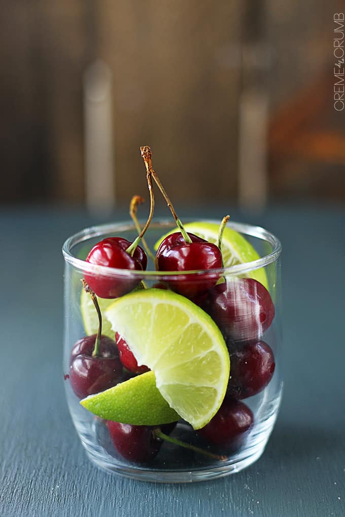 a small glass full of cherries and slices of limes.