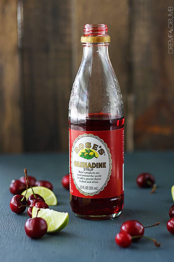 a bottle of Rose's grenadine syrup surrounded by cherries and lime slices.