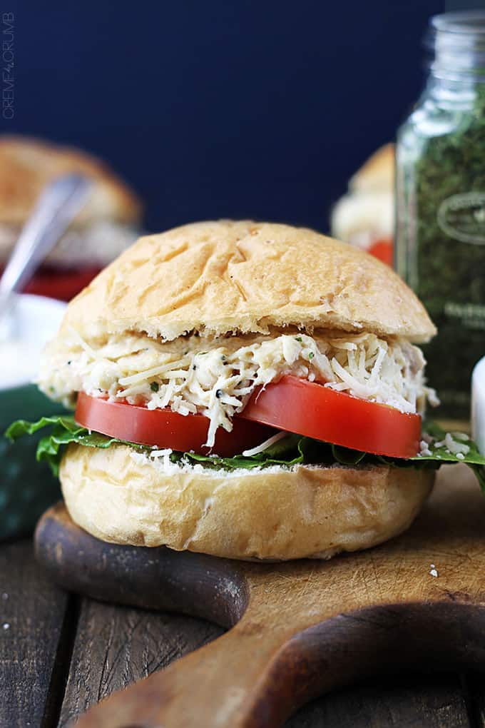 a slow cooker chicken caesar slider on a wooden cutting board with ingredients and more slides faded in the background.